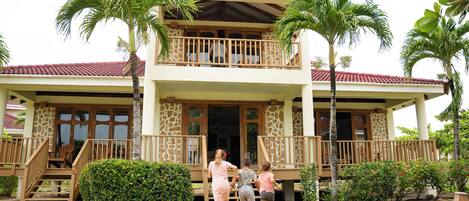 A two-story building with a balcony, palm trees, and a pathway leading to the entrance.