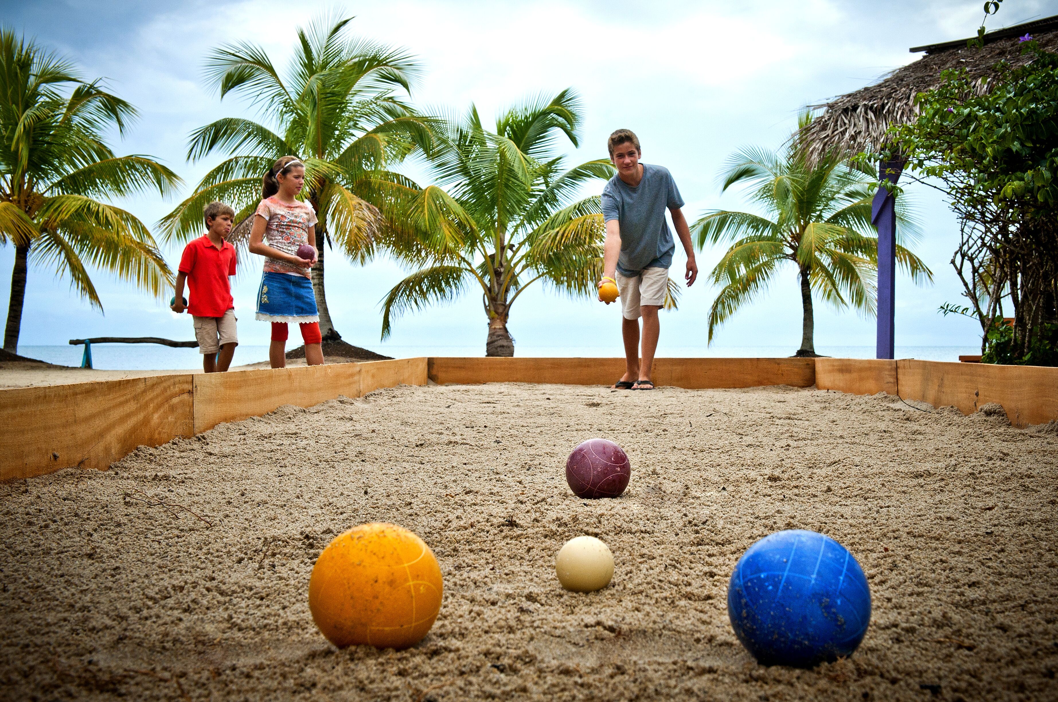 Ein Strandabschnitt mit Sand, Palmen und einer Holzkonstruktion.