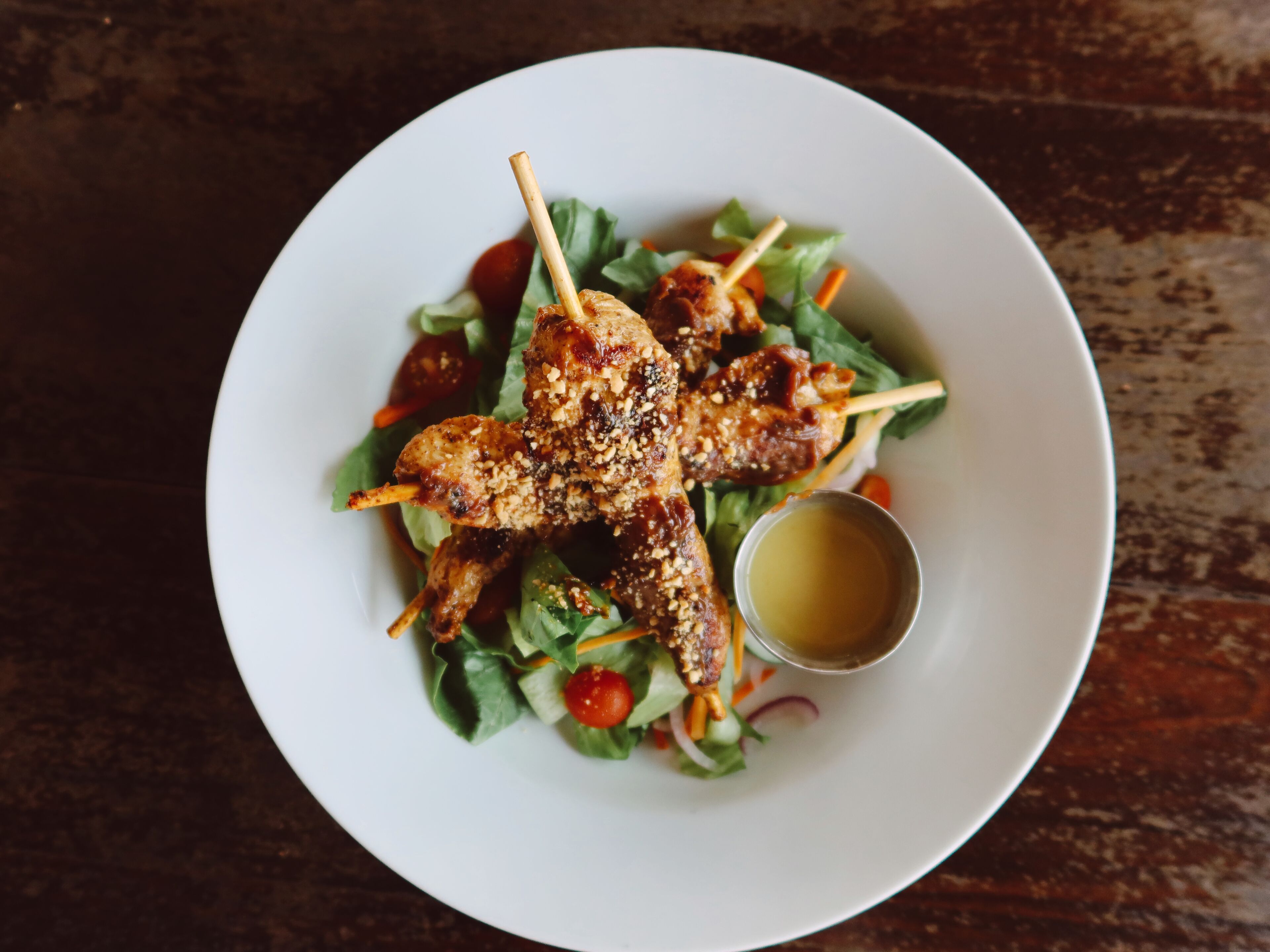 A plate of grilled skewers with a side of salad and a small bowl of sauce.