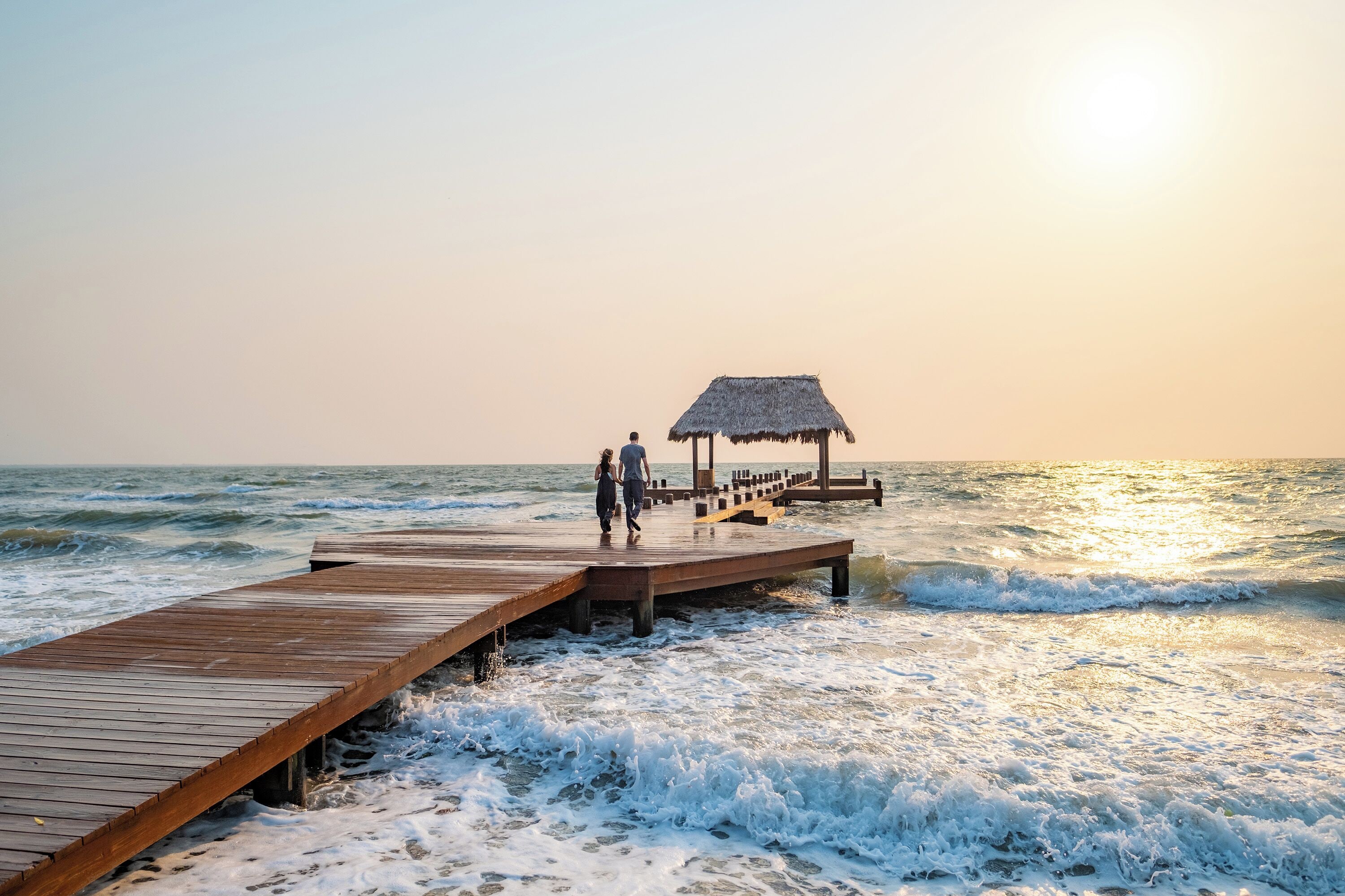 A wooden pier extending into the ocean with a thatched-roof structure at the end.