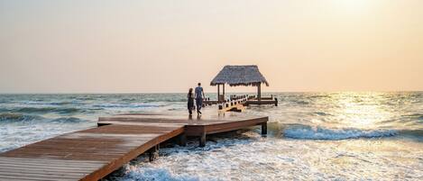 A wooden pier extending into the ocean with a thatched-roof structure at the end.