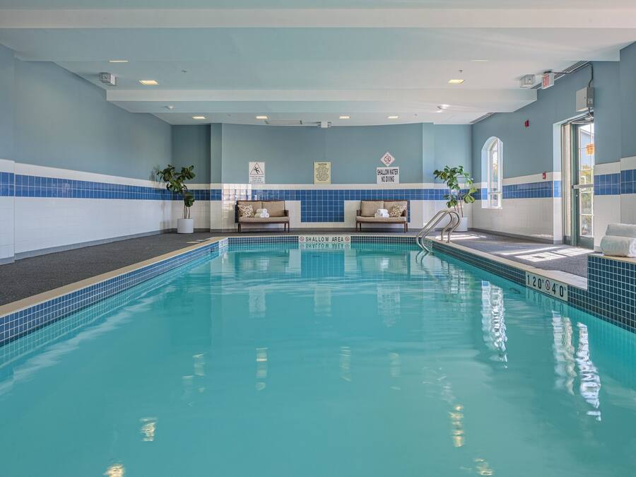 An indoor swimming pool with a tiled floor, benches, and safety signs.