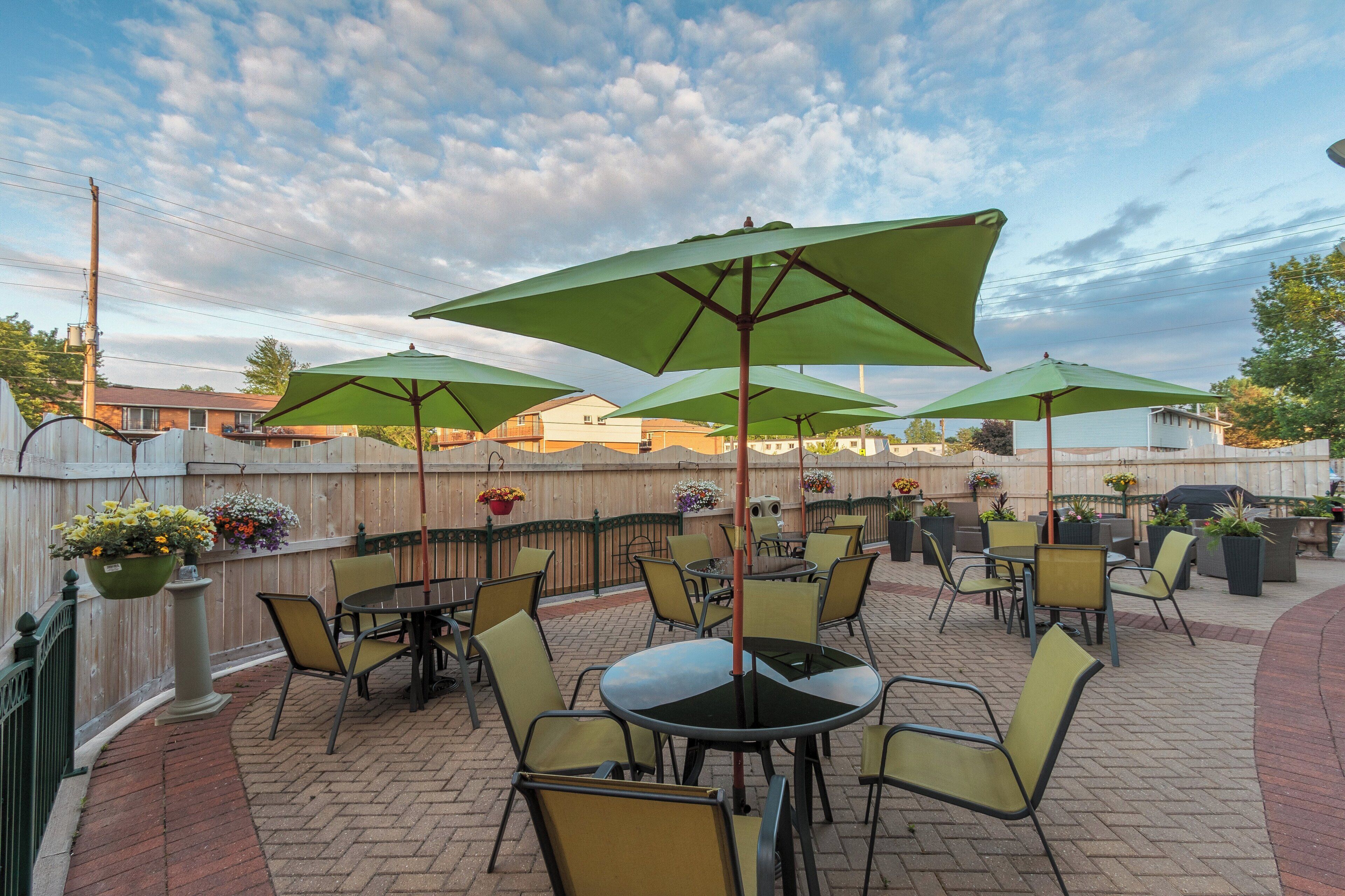 An outdoor patio with tables and chairs, green umbrellas, and hanging flower baskets.