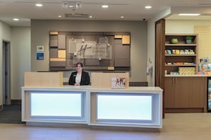 A reception desk with a Holiday Inn Express & Suites sign, a welcome poster, and a security camera above. - Holiday Inn Express & Suites Belleville by IHG (Belleville)
