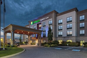 Edificio de Holiday Inn Express & Suites con entrada cubierta, estacionamiento y asta con bandera.