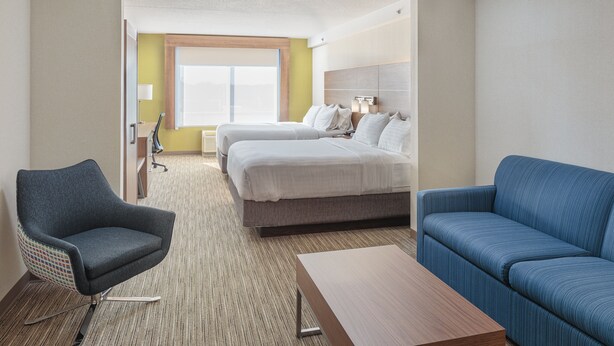Une chambre d’hôtel avec un lit, deux chaises, un canapé, une table en bois et une fenêtre donnant sur un paysage agréable.