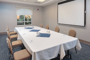 A conference room with a long table, chairs, a projector screen, and a window with a view of greenery. - Holiday Inn Express & Suites Belleville by IHG (Belleville)