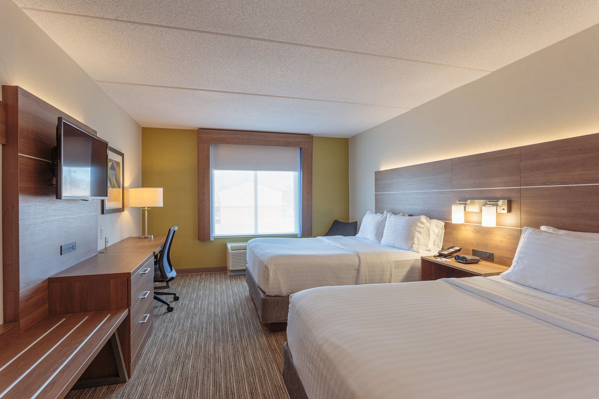 A hotel room with two beds, a desk with a chair, a television, and a window with blinds.