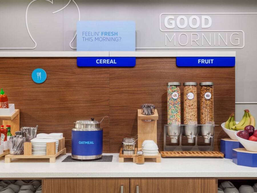 A breakfast bar with cereal and fruit options, a kettle, and condiments.