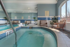 An indoor swimming pool with a tiled edge, lounge chairs, and a window with a view. - Holiday Inn Express & Suites Belleville by IHG (Belleville)
