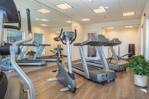 Une salle de sport équipée de plusieurs tapis de course, de vélos d’appartement et d’un support pour les poids.