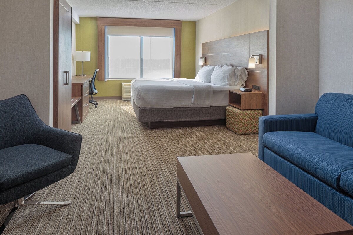 A hotel room with a bed, a desk, a chair, a sofa, and a window.