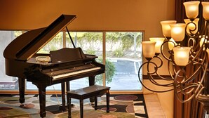 A grand piano in a room with large windows, a patterned carpet, and a decorative chandelier. - Best Western Route 66 Glendora Inn (Glendora)