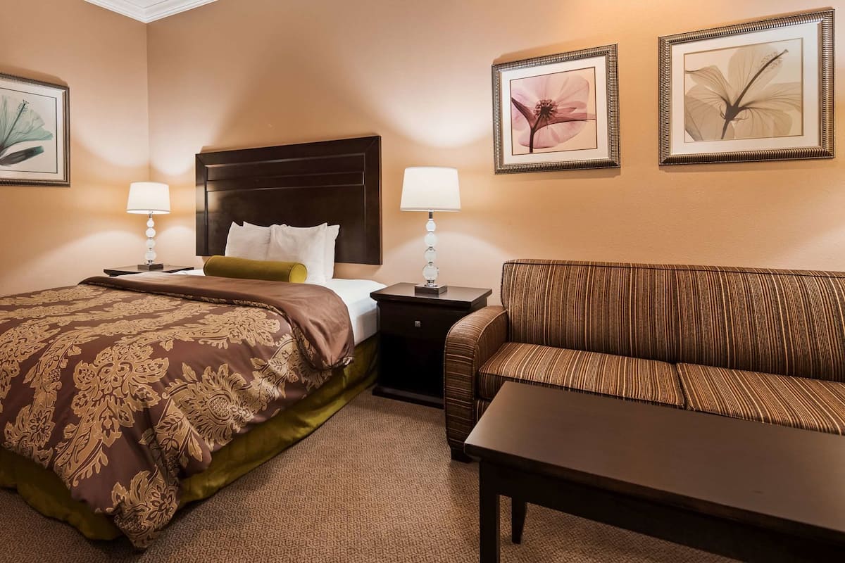 A hotel room with a bed, a sofa, two bedside lamps, and three framed artworks on the walls.