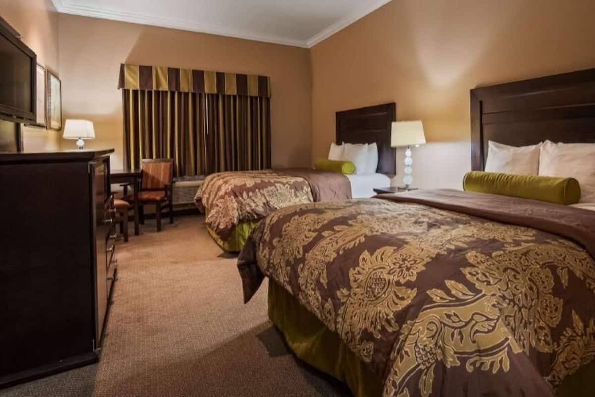 A hotel room with two beds, a desk, a chair, and a television.