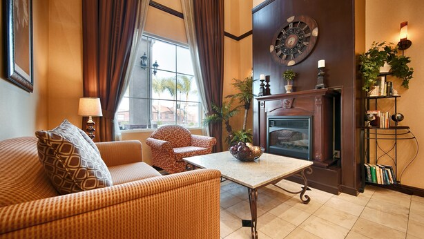 A cozy living room with a sofa, armchair, and a fireplace. - Best Western Route 66 Glendora Inn (Glendora)