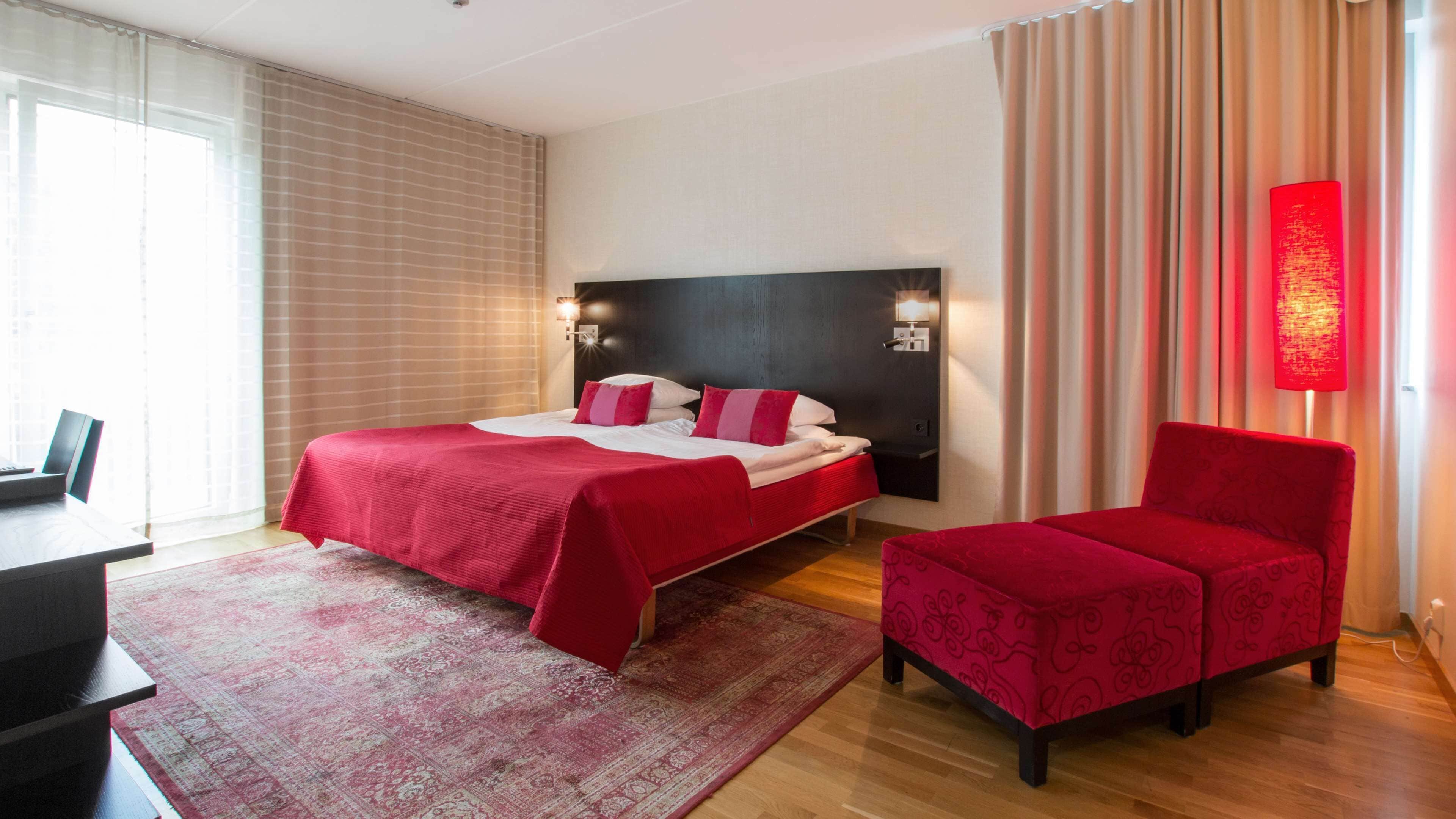 Una camera d'albergo con un letto, una scrivania, una sedia e un'ampia finestra con tende.