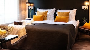 Una cama bien hecha con almohadas blancas y mostaza, un cabecero oscuro y lámparas de noche.