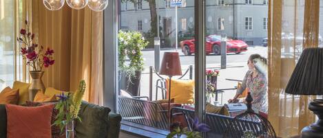 A cozy interior with a sofa, cushions, a table, and a window overlooking a street with cars and a pedestrian crossing sign.