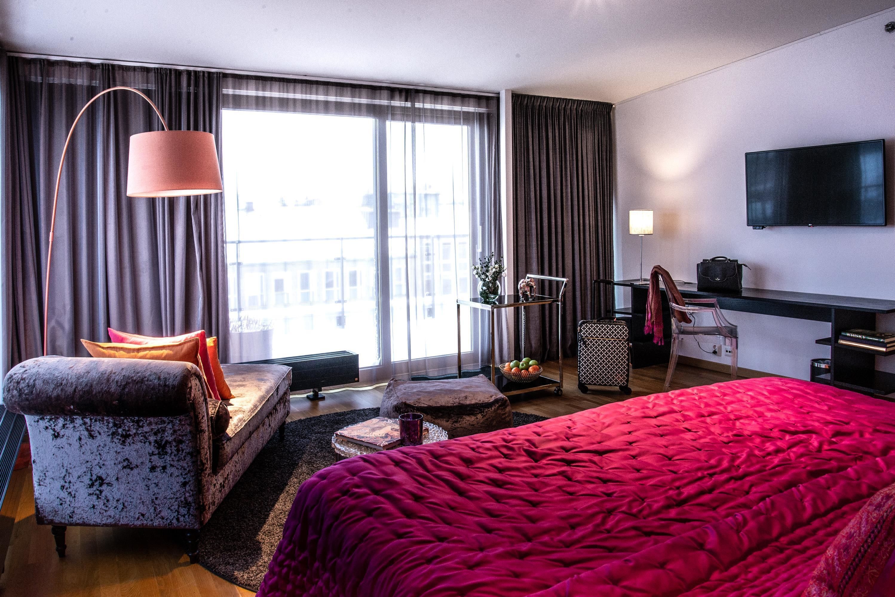 A modern hotel room with a large bed, a sofa, a desk, and a TV.