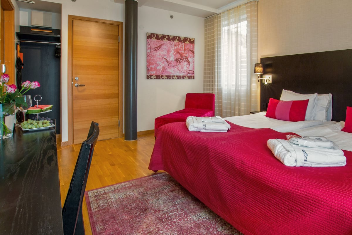A hotel room with a large bed, a red chair, a wooden door, and a painting on the wall.