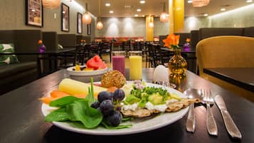 Un desayuno con un plato de comida, que incluye frutas, verduras y un croissant, en un restaurante con cabinas e iluminación colgante.