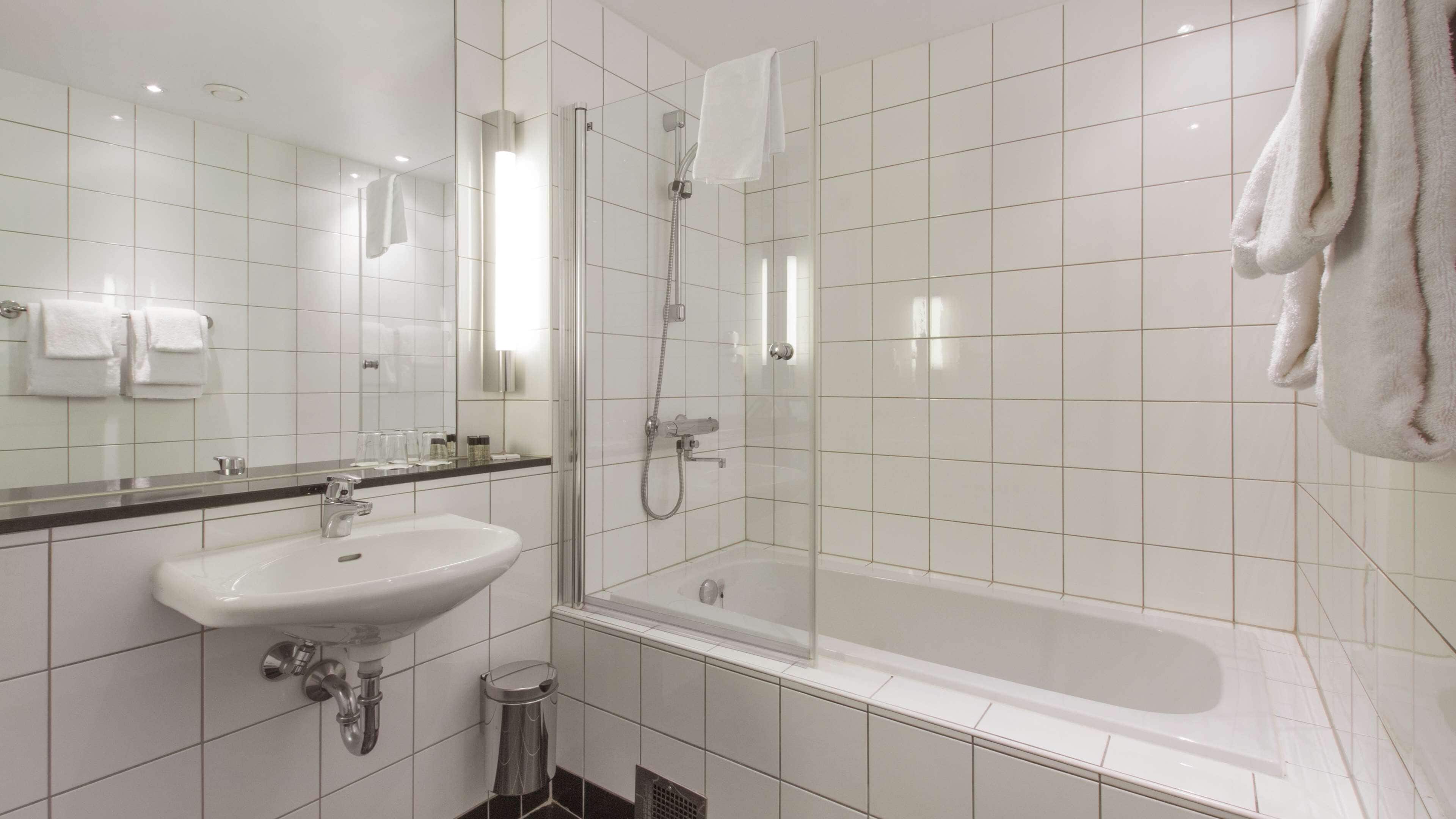 A modern bathroom with a white sink, mirror, and bathtub.