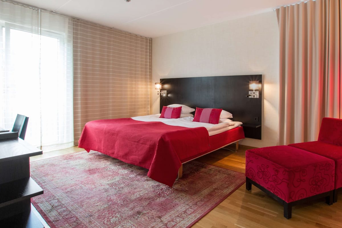 A hotel room with a large bed, a desk, and a chair.