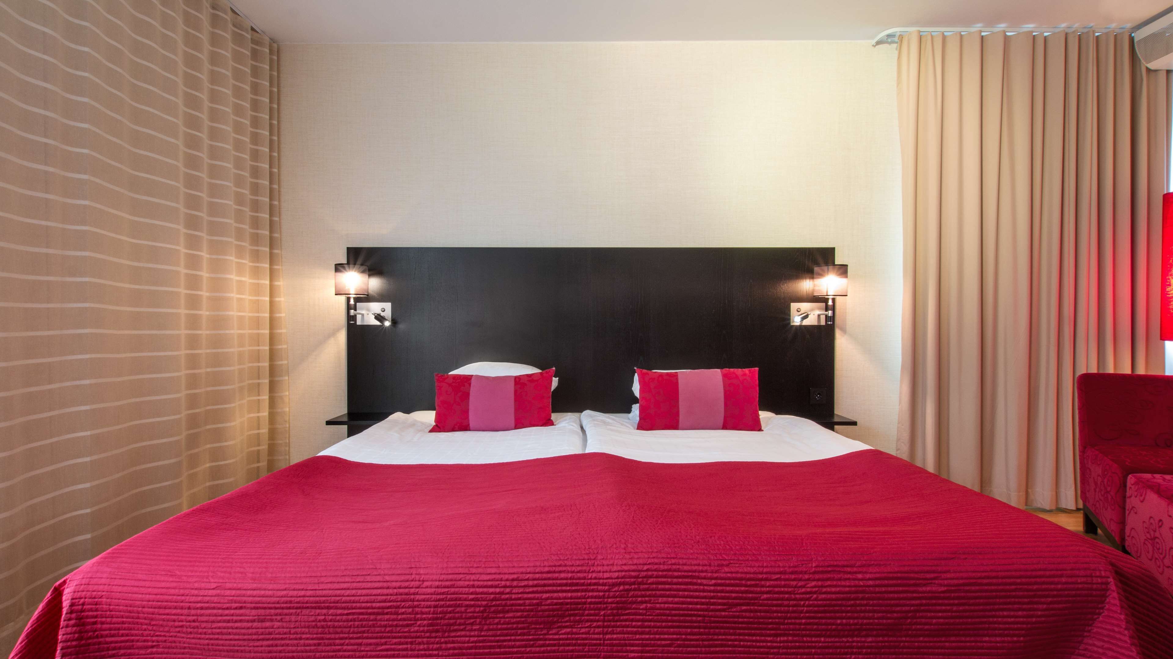 A hotel room with a large bed, two bedside tables with lamps, a headboard, and a window with curtains.