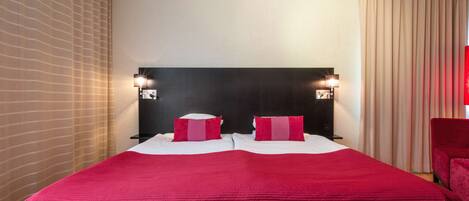 A hotel room with a large bed, two bedside tables with lamps, a headboard, and a window with curtains.