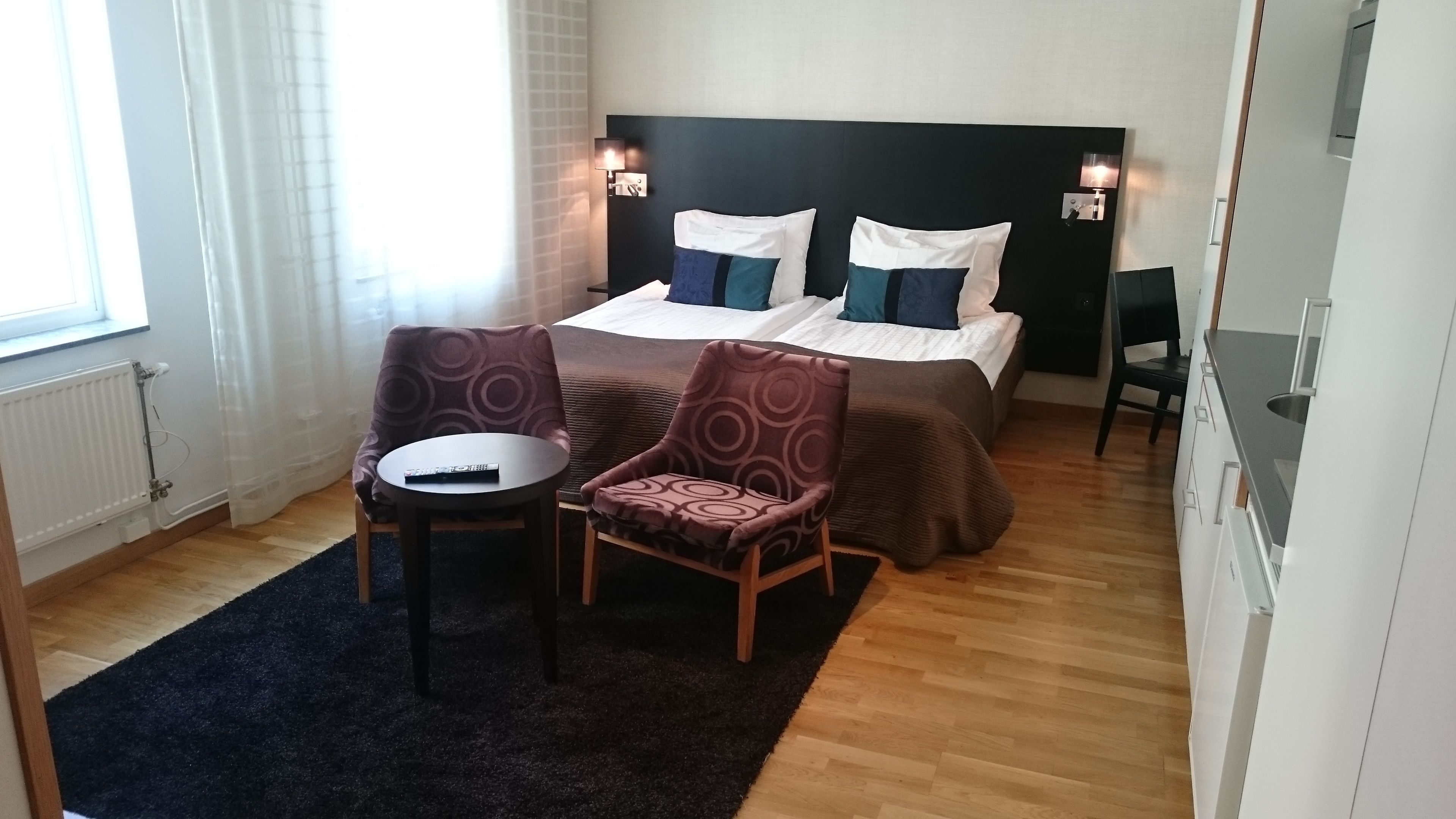 A hotel room with a bed, two armchairs, a small table, and a nightstand.