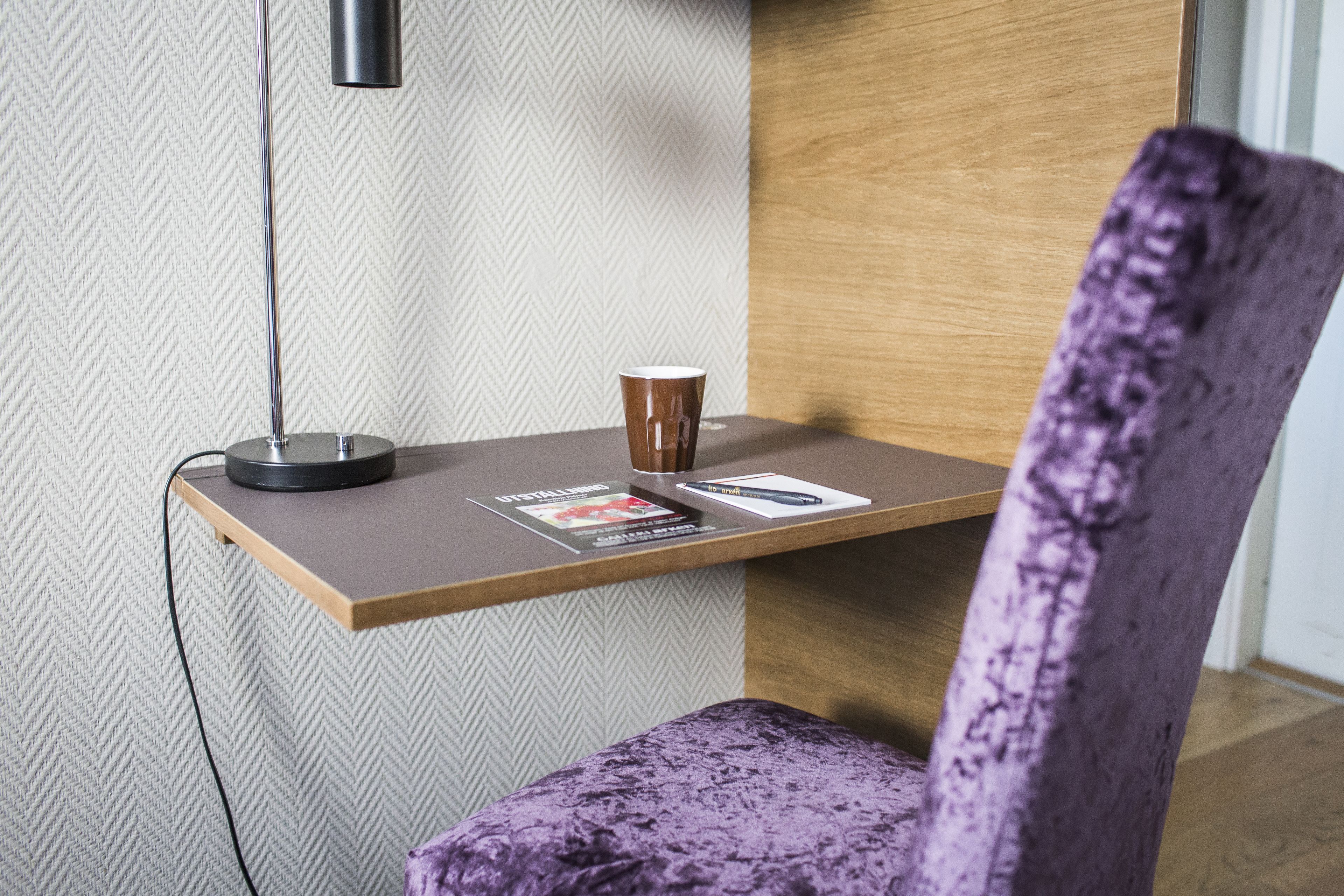 A wooden desk with a lamp, a purple chair, and a magazine on it.