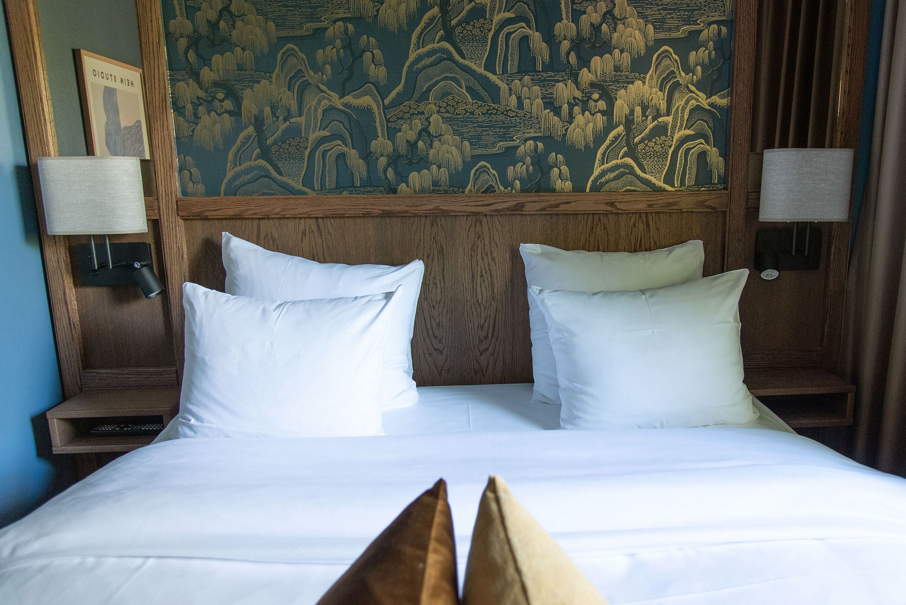 Una habitación de hotel con una cama grande, dos lámparas de noche y una pared decorada con un tapiz tradicional.