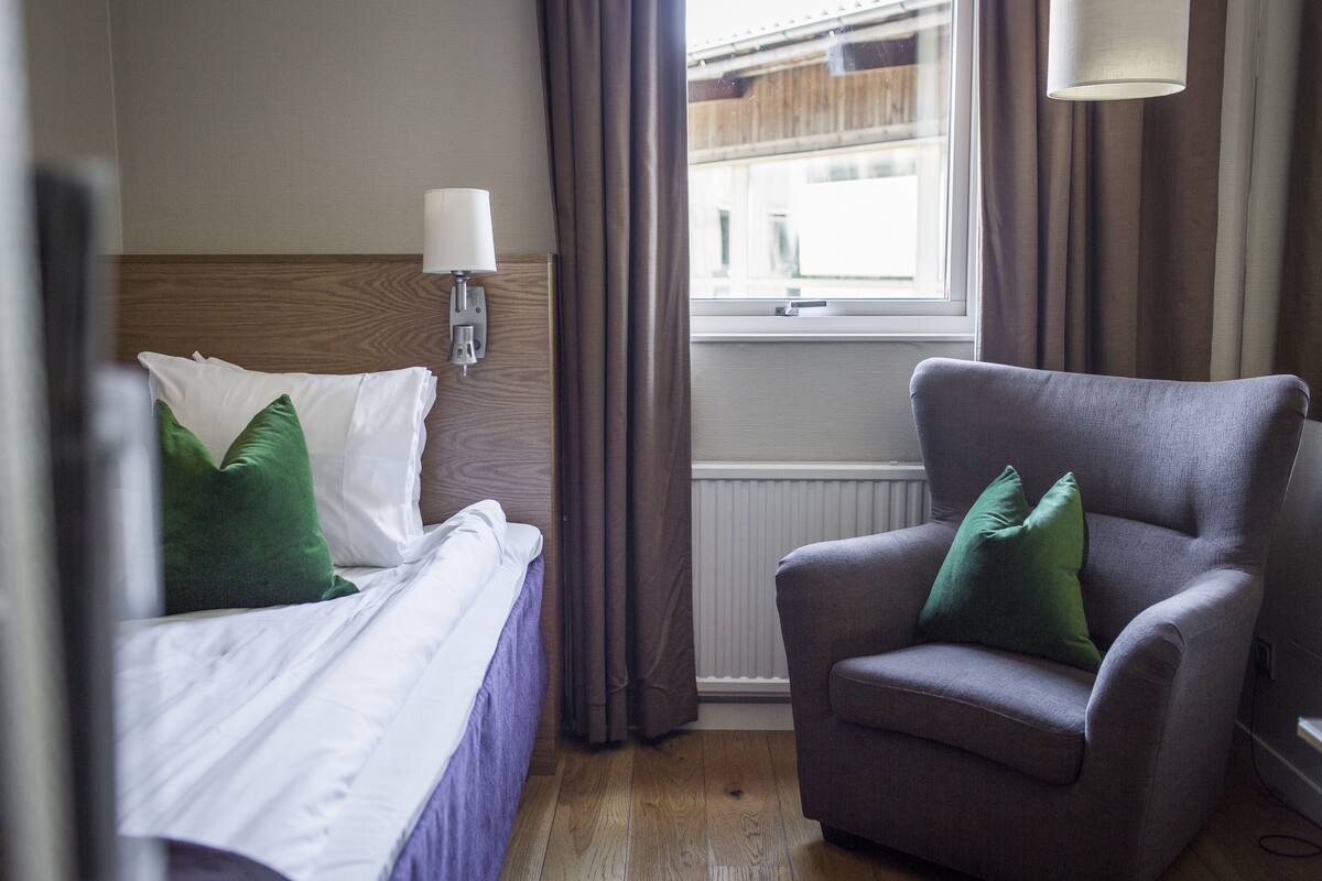 Una habitación de hotel con una cama, una silla, un ventanal y una lámpara.
