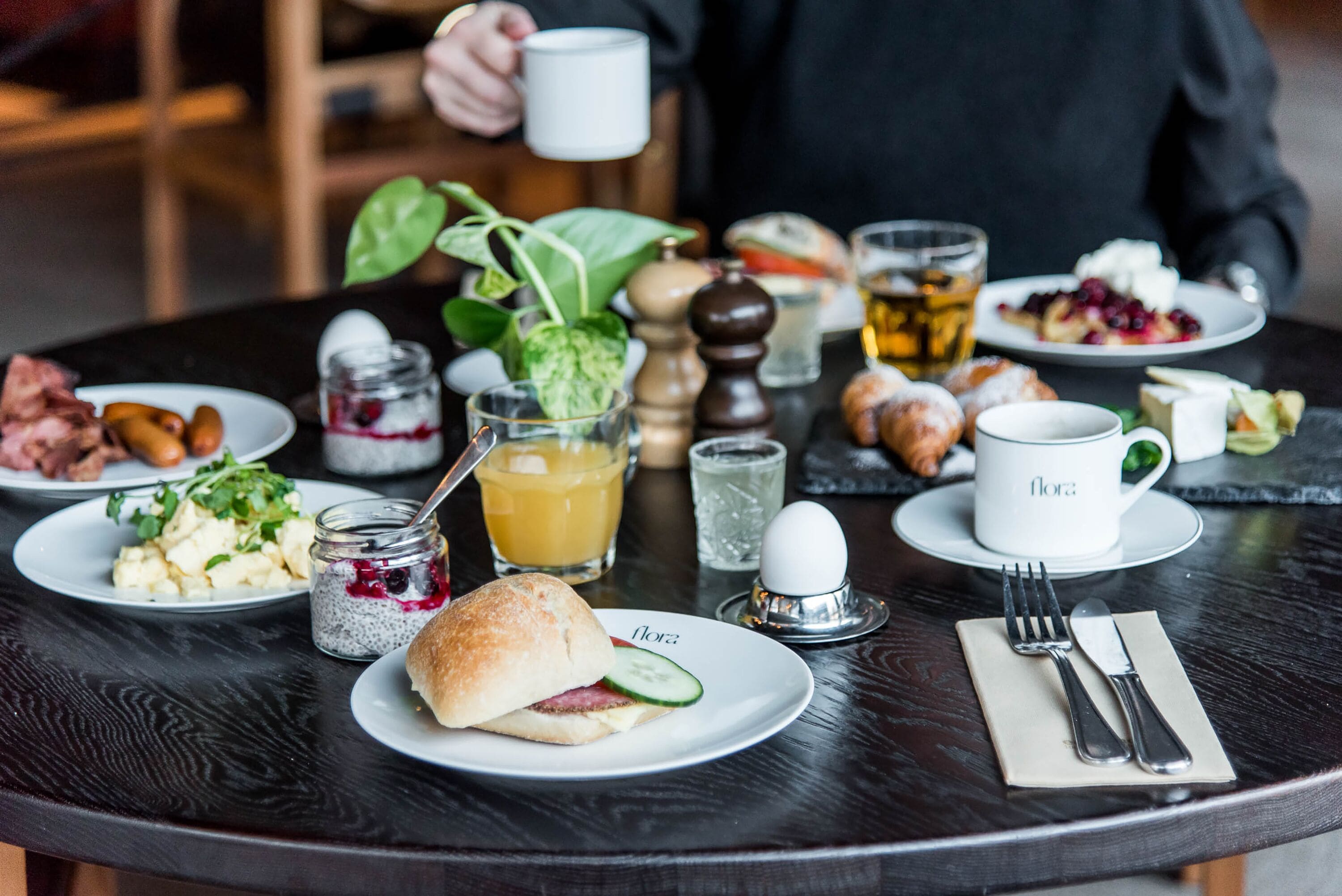 A breakfast setting with various dishes, including a sandwich, a bowl of fruit, and a cup of tea.