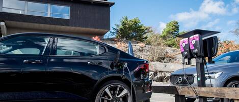 A black car parked at a charging station with a building in the background.