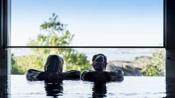 To personer i jacuzzi med udsigt til træer og vand.