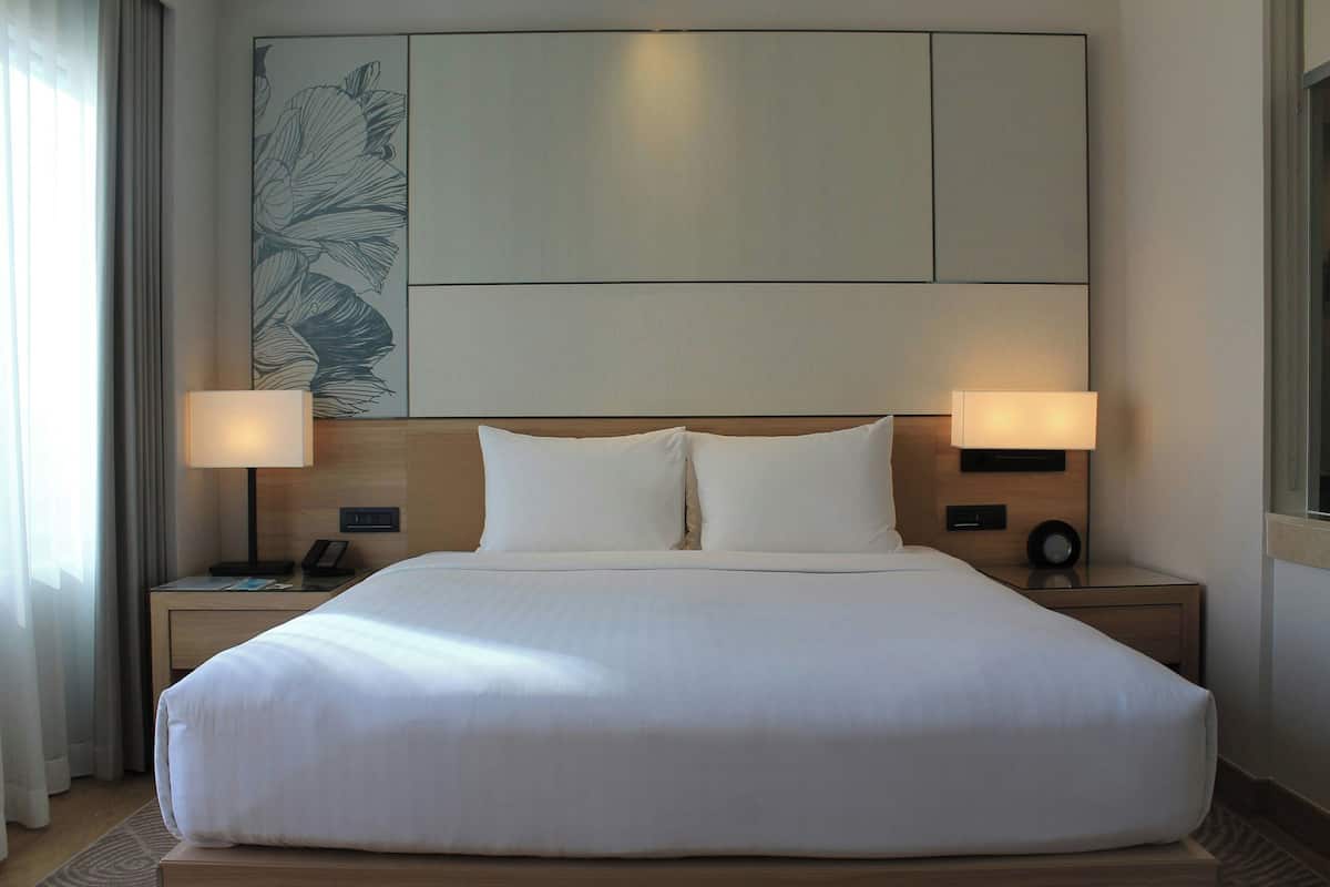 Una cama grande con ropa blanca, dos mesitas de noche con lámparas, una obra de arte en la pared y una paleta de colores neutros.