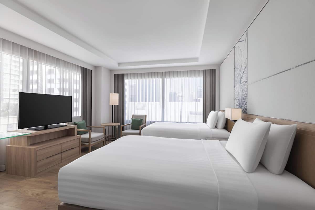 Una habitación de hotel moderna con dos camas, un televisor de pantalla plana, un escritorio y una silla.