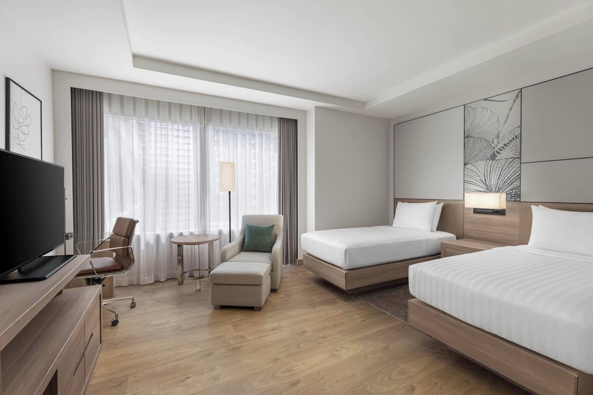 Una habitación de hotel con una cama, un escritorio con televisor, una silla, una mesita y una lámpara.