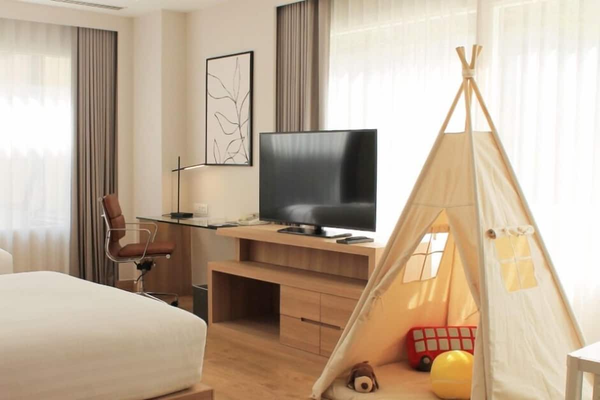 Una habitación de hotel con cama, escritorio con televisor, silla, tienda de campaña y juguetes.