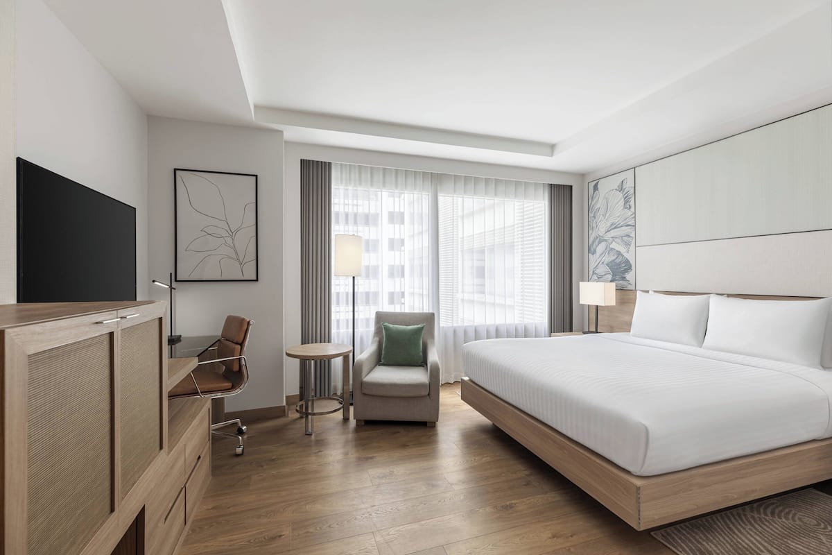 Una habitación de hotel moderna con una cama grande, un escritorio con una silla, una mesita y un televisor.