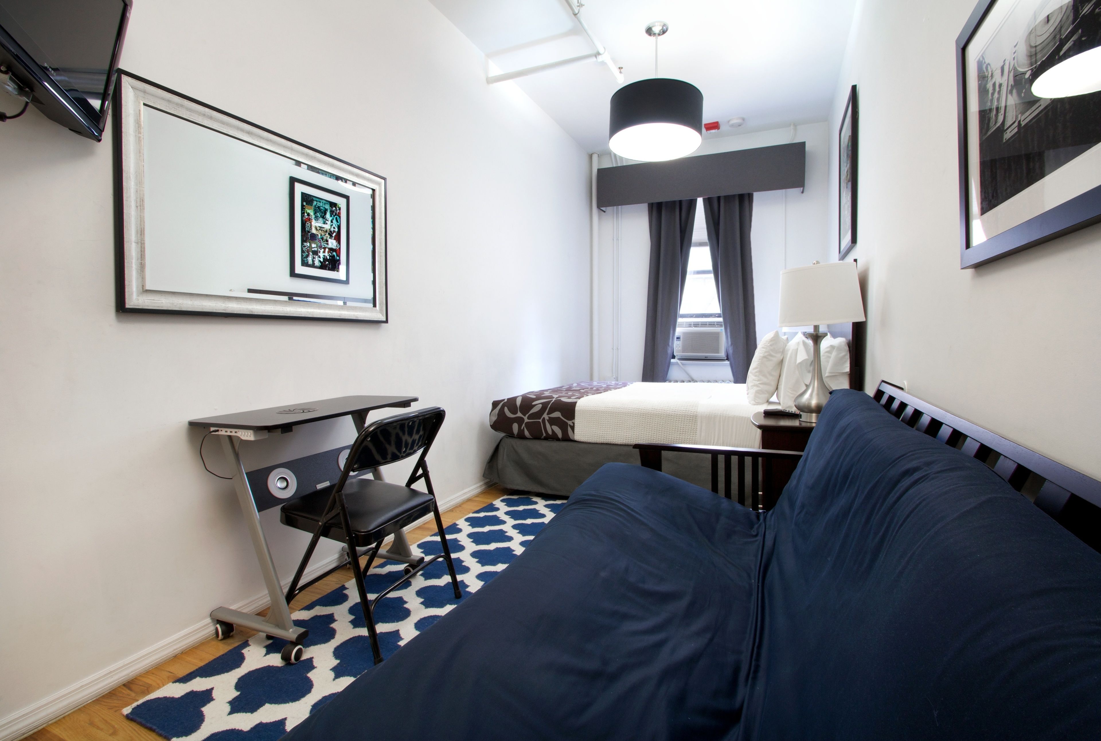 Une chambre d’hôtel de taille réduite, comprenant un lit, un bureau, une chaise et une petite table.