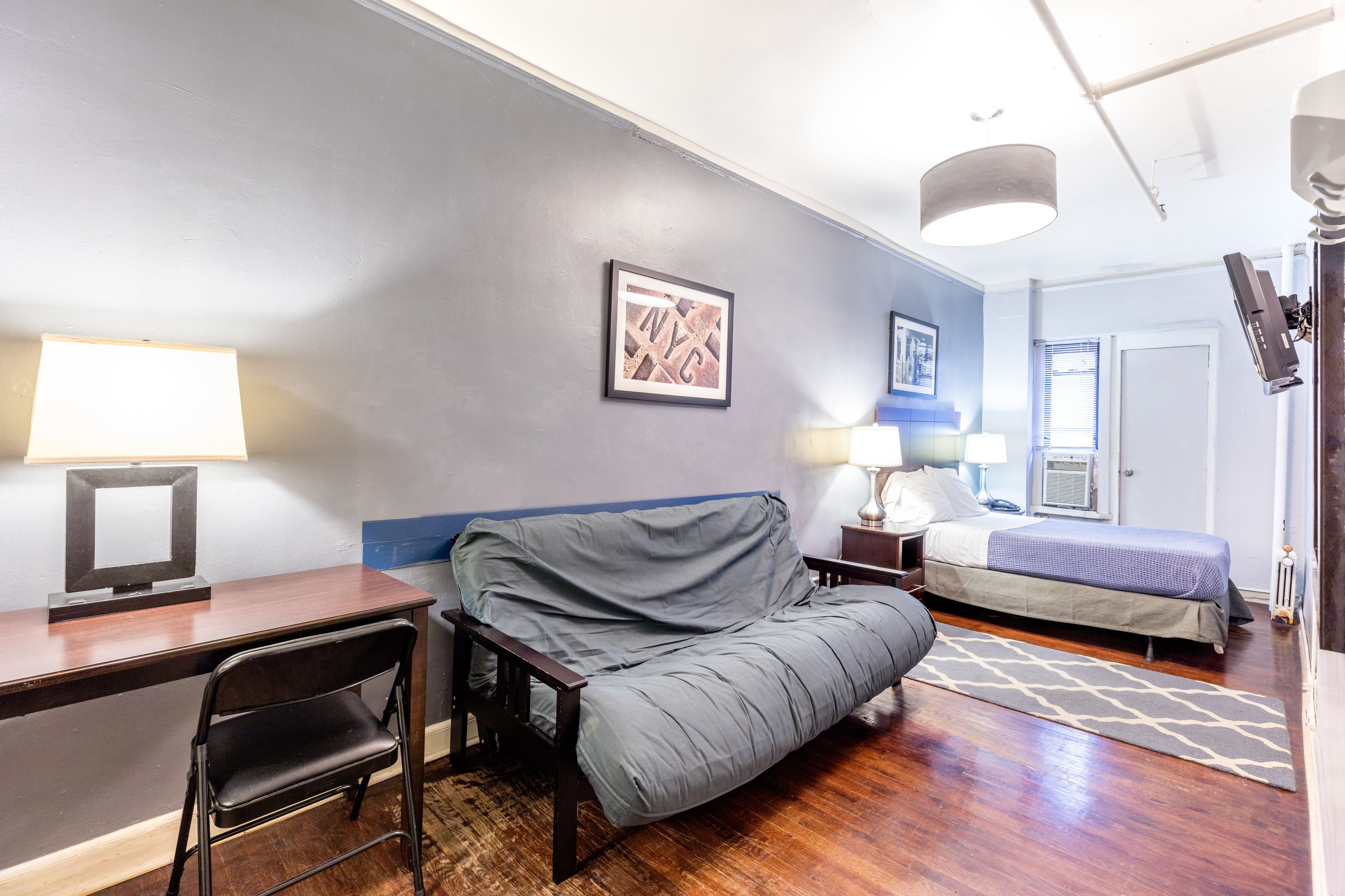 A compact hotel room with a desk, chair, sofa, and a bed.