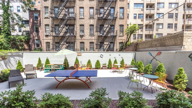 An outdoor patio with a ping pong table, seating, and small trees.