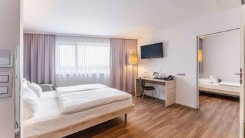 Habitación de hotel con cama, escritorio, silla, televisor y una pequeña zona de estar.