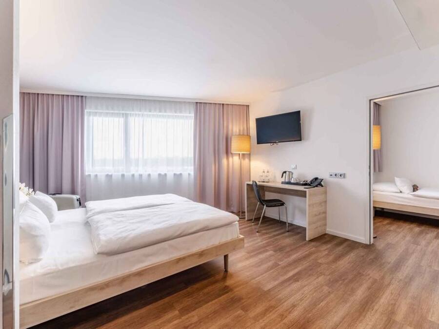 Habitación de hotel con cama, escritorio, silla, televisor y una pequeña zona de estar.