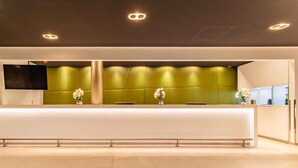 A reception area with a long counter, a flat-screen TV, and two flower vases.