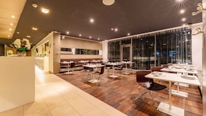A modern restaurant with a mix of booth and table seating, a wooden floor, and large windows.