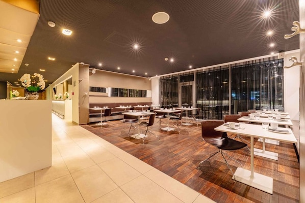 Un restaurante moderno con una combinación de asientos tipo cabina y mesas, piso de madera y amplios ventanales.